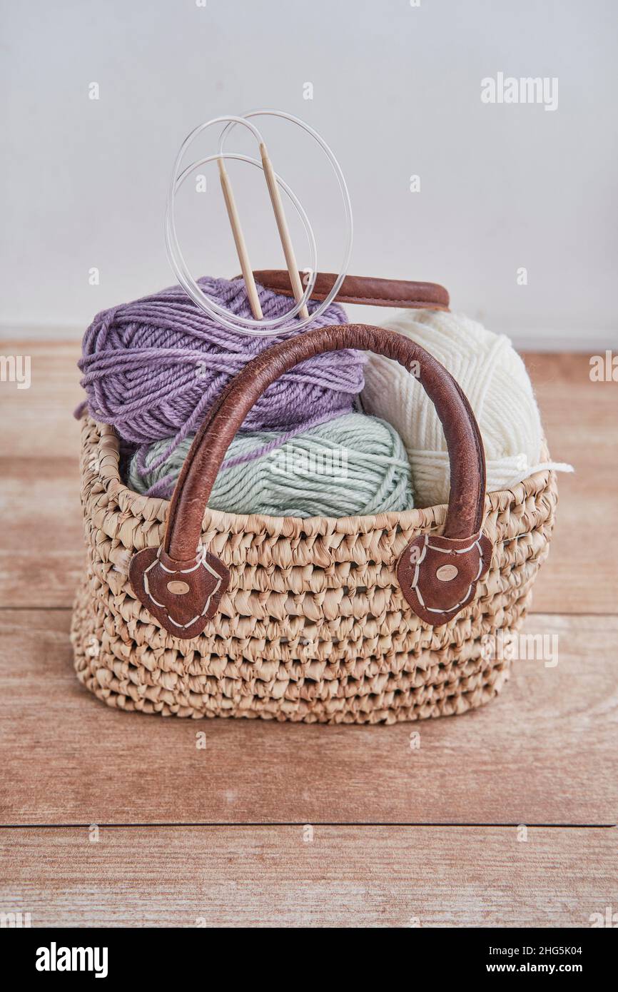 Skeins of yarn, wooden circular knitting needles in handmade straw basket on wooden table Stock Photo