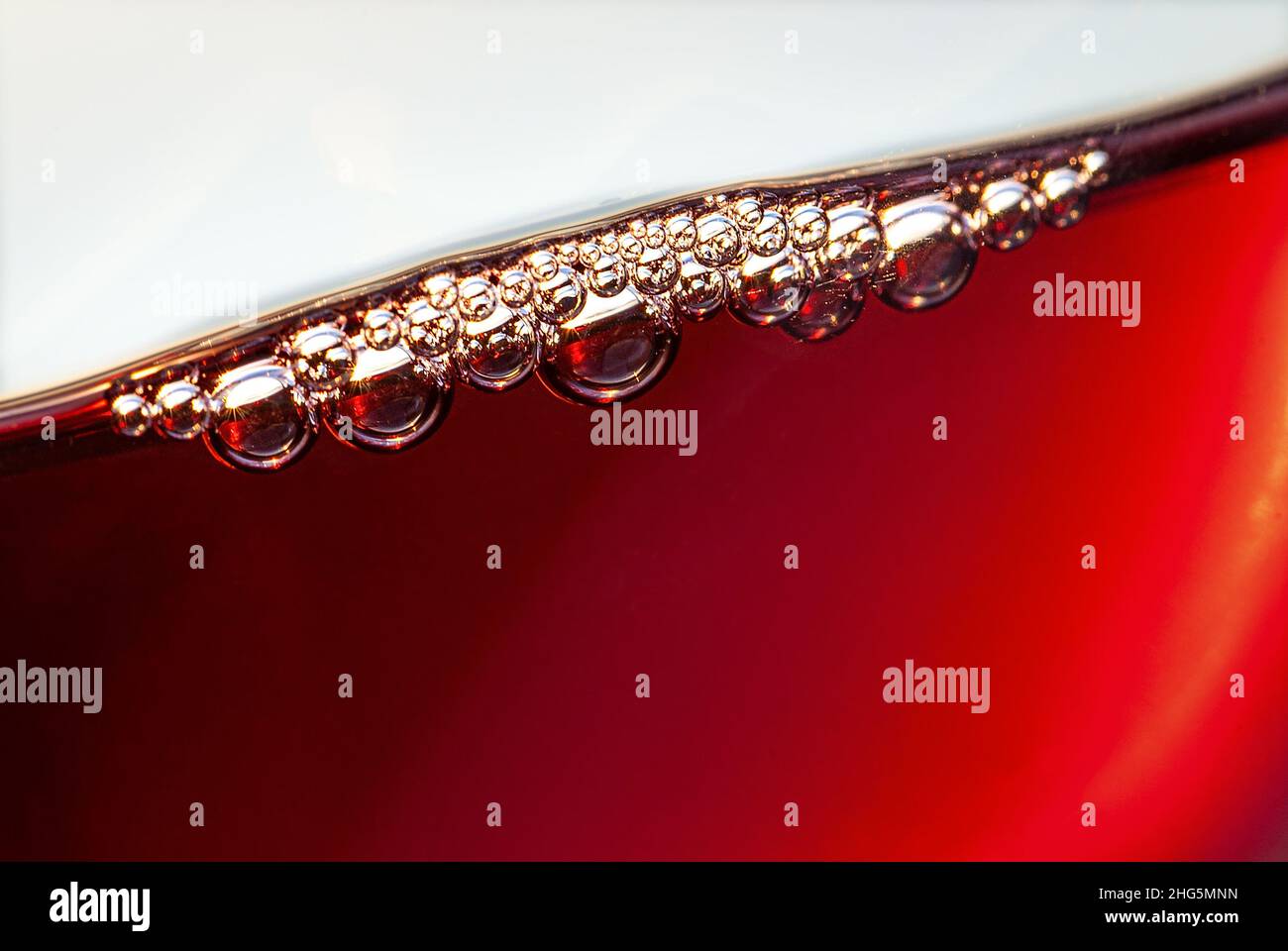 Wine aeration bubbles forming on surface in a freshly poured aerated glass of red wine adding a fuller taste to young and inexpensive wines, back-lit by setting sun Stock Photo
