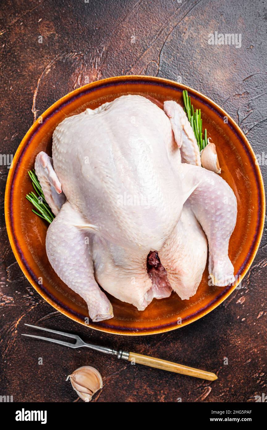 Chicken, raw poultry in a rustic plate with rosemary. Dark background