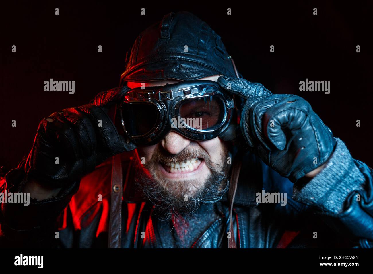 Portrait of retro angry driver with beard wearing vintage glasses and leather helmet. Blue and red fill light. Automotive retro nostalgy concept Stock Photo