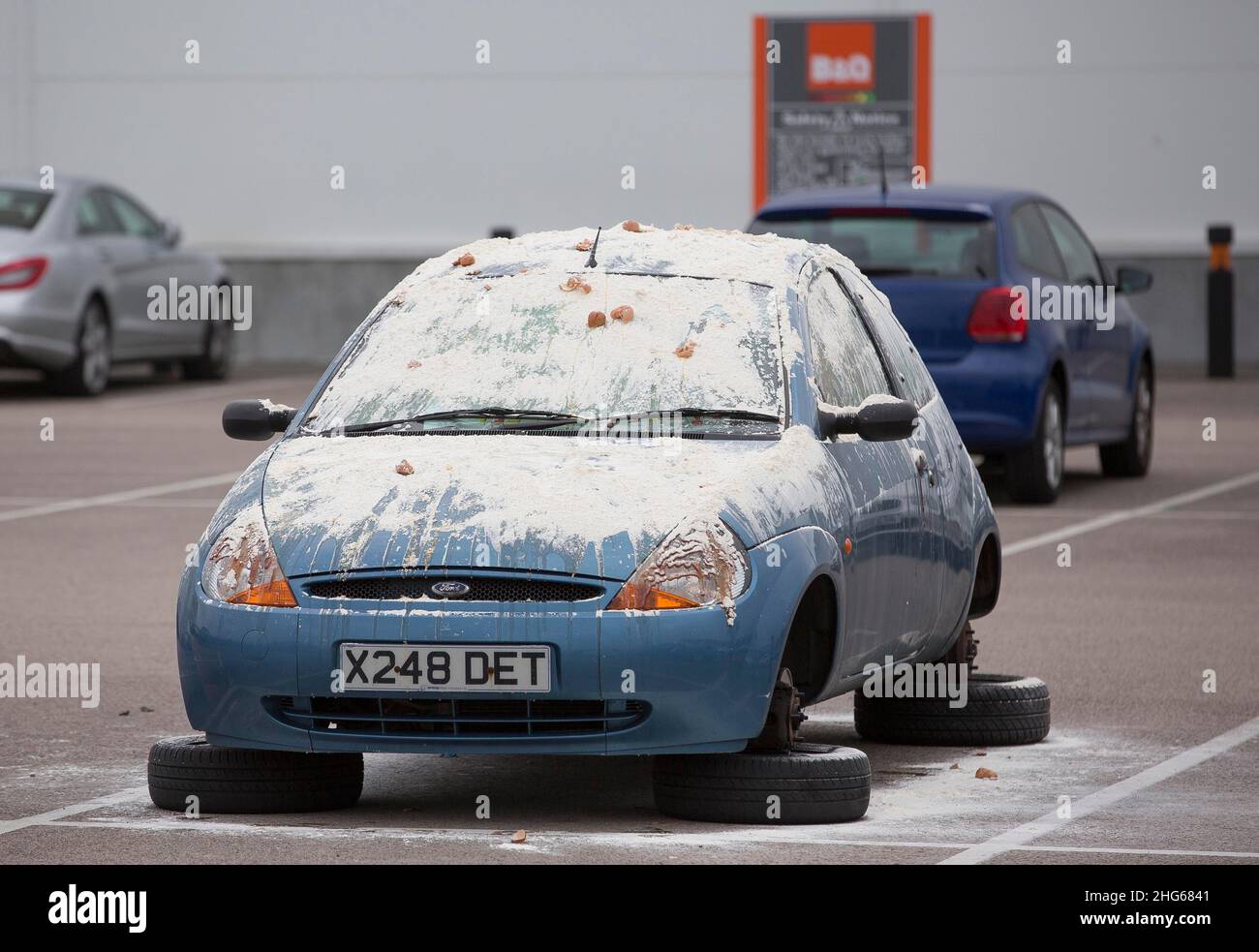 Ford Ka covered in eggs and flour with wheels removed in a shopping centre car park Stock Photo