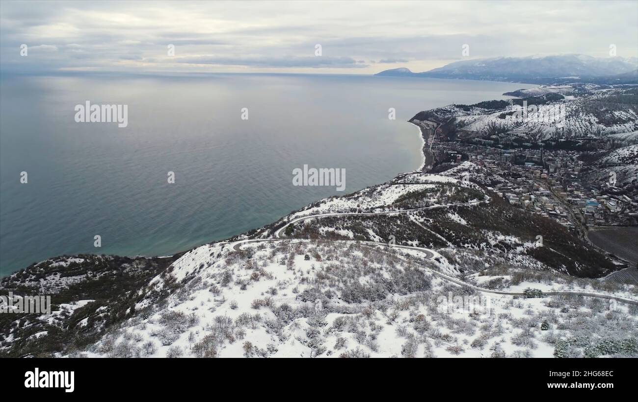 Beautiful winter seascape with snowy fields, forest and blue sea on grey, cloudy sky background. Aerial for winter coastline with snowy trees and fiel Stock Photo