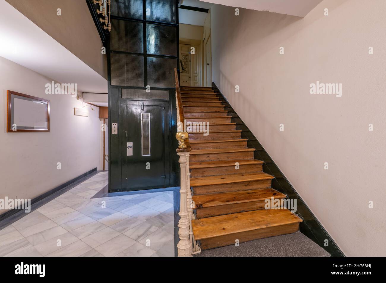 Portal of an old building with wooden stairs and green metal elevator with white marble floors Stock Photo