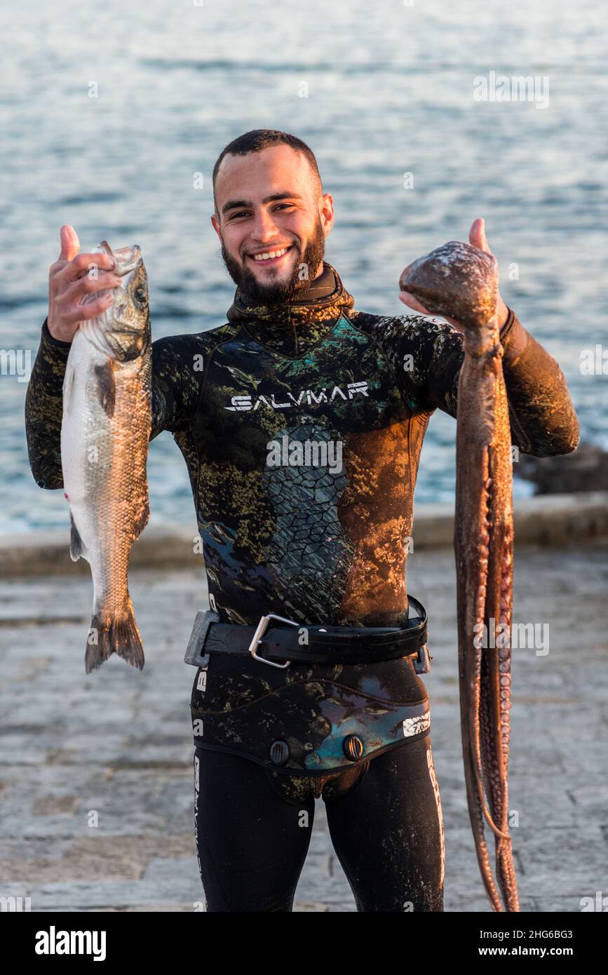 Cascais, Portugal - Young Portuguese man proudly holding up fresh catch off the coast of Cascais, Portugal - spearfishing Stock Photo