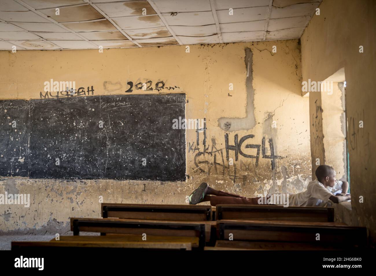 A boy seen laying on a desk in an empty classroom of Moduganari primary