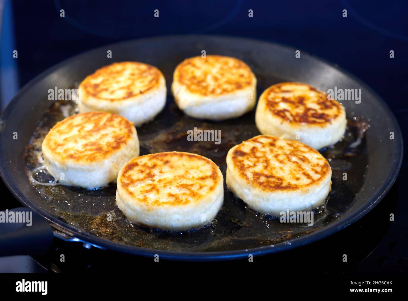 Cottage cheesecakes are fried in a frying pan. The process of cooking delicious homemade food. cheese pancakes or syrniki. Stock Photo