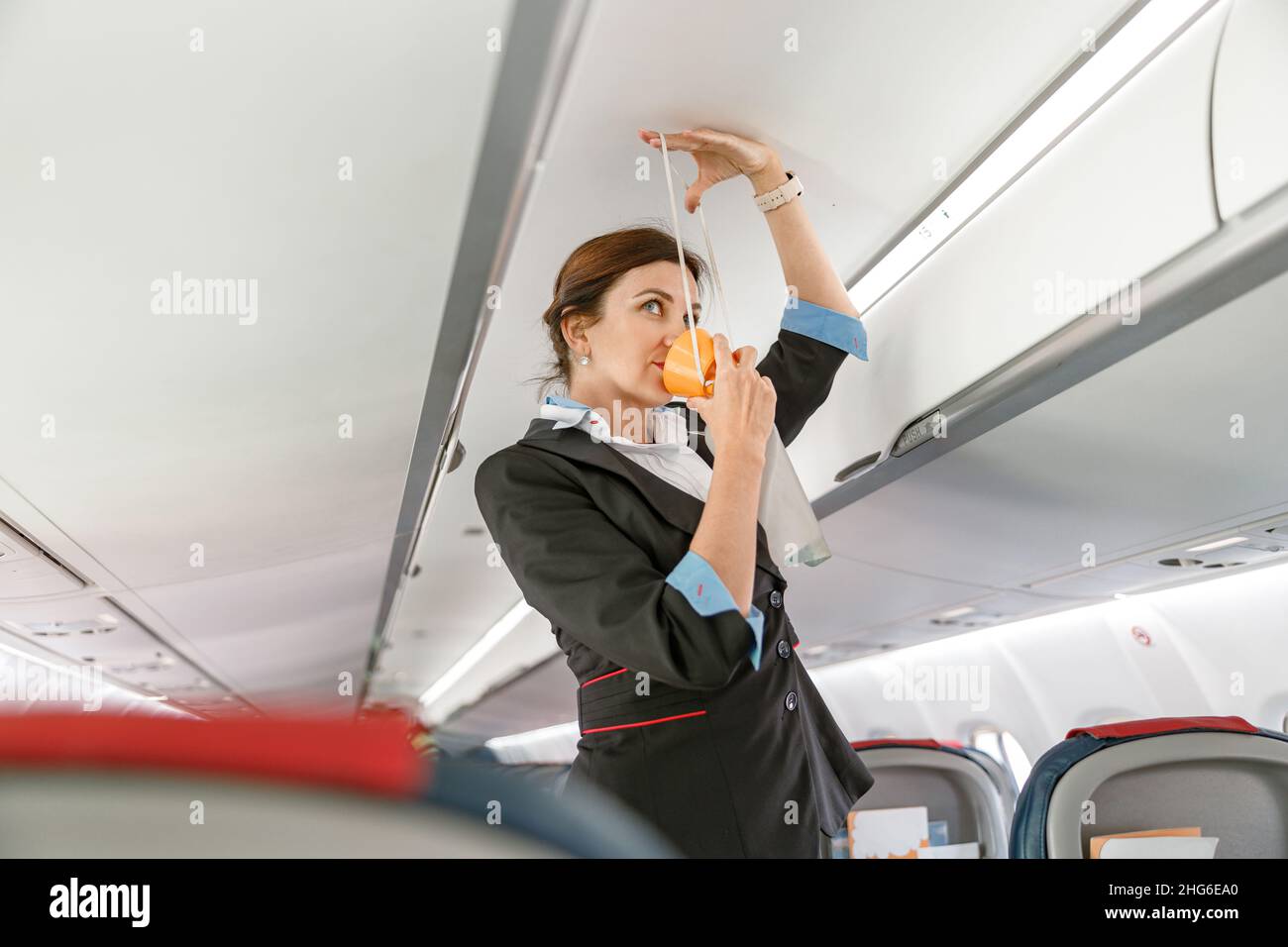 Flight attendant demonstrating how to use oxygen mask in airplane Stock