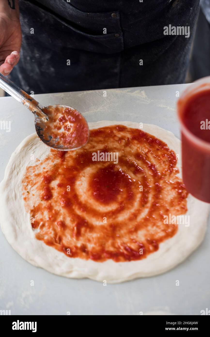 Pizza maker spreading sauce on pizza base Stock Photo Alamy