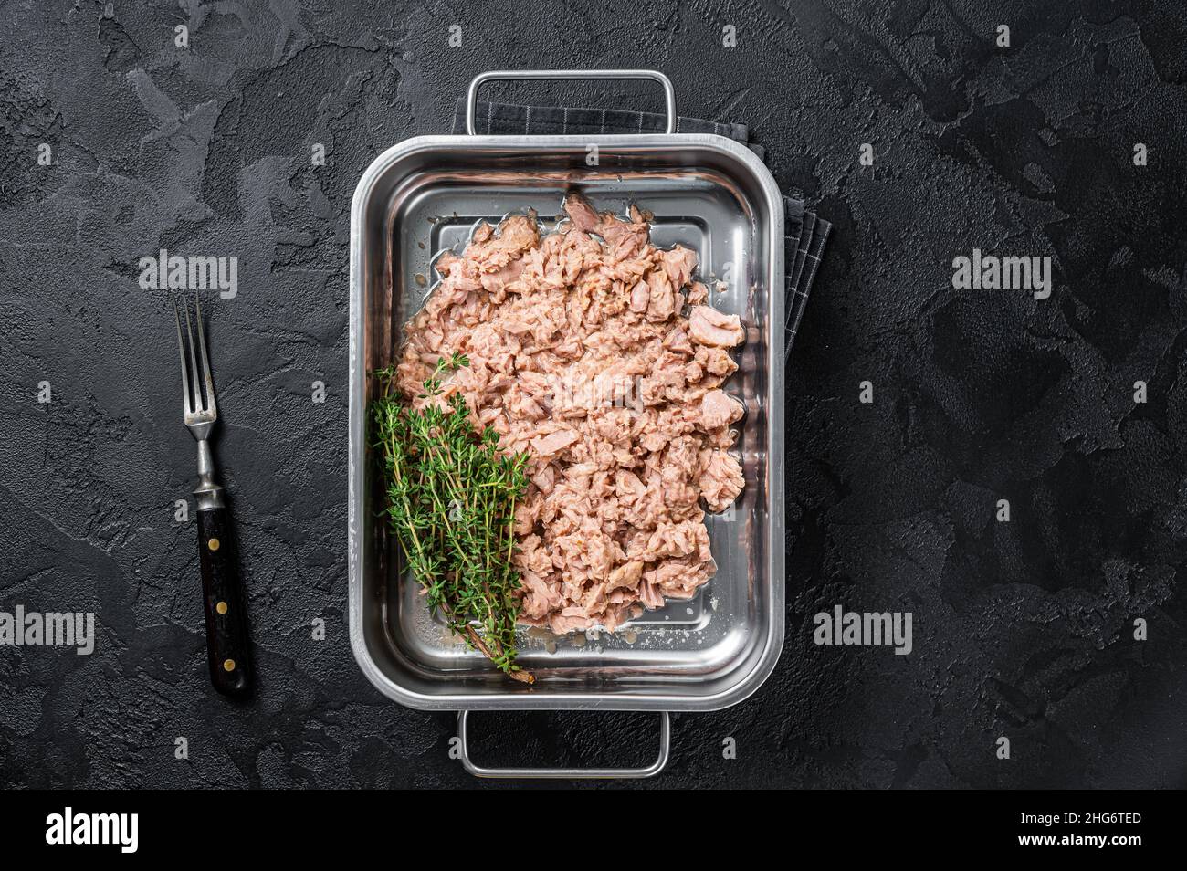 Tuna canned fish with olive oil in a tray . Black background. top view