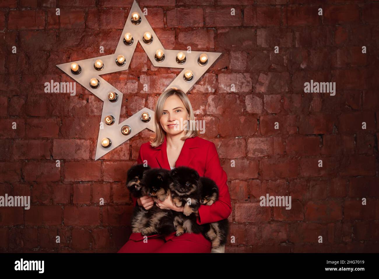 Smiling pretty business woman in red jacket holding cute puppies of pomeranian spitz breed dog. Owner or breeder with litter of puppies. Stock Photo