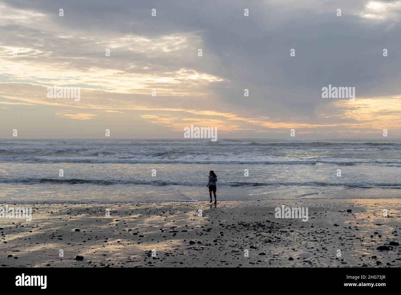 A young woman runs from wave during sunset on the beach in Oceanside, Oregon, on Sunday, January 16, 2022. Pacific tsunami threat triggered by a massive... Stock Photo