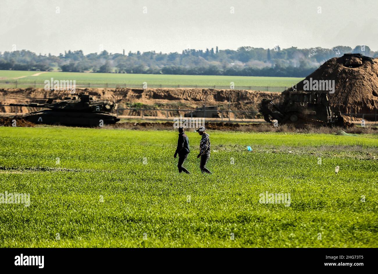 Gaza, Palestine. 18th Jan, 2022. Farmers work on a farm near the fence separating Gaza and Israel, while Israeli military vehicles bulldoze parts of Palestinian agricultural land in Khuza'a, east of Khan Yunis, in the southern Gaza Strip. Credit: SOPA Images Limited/Alamy Live News Stock Photo