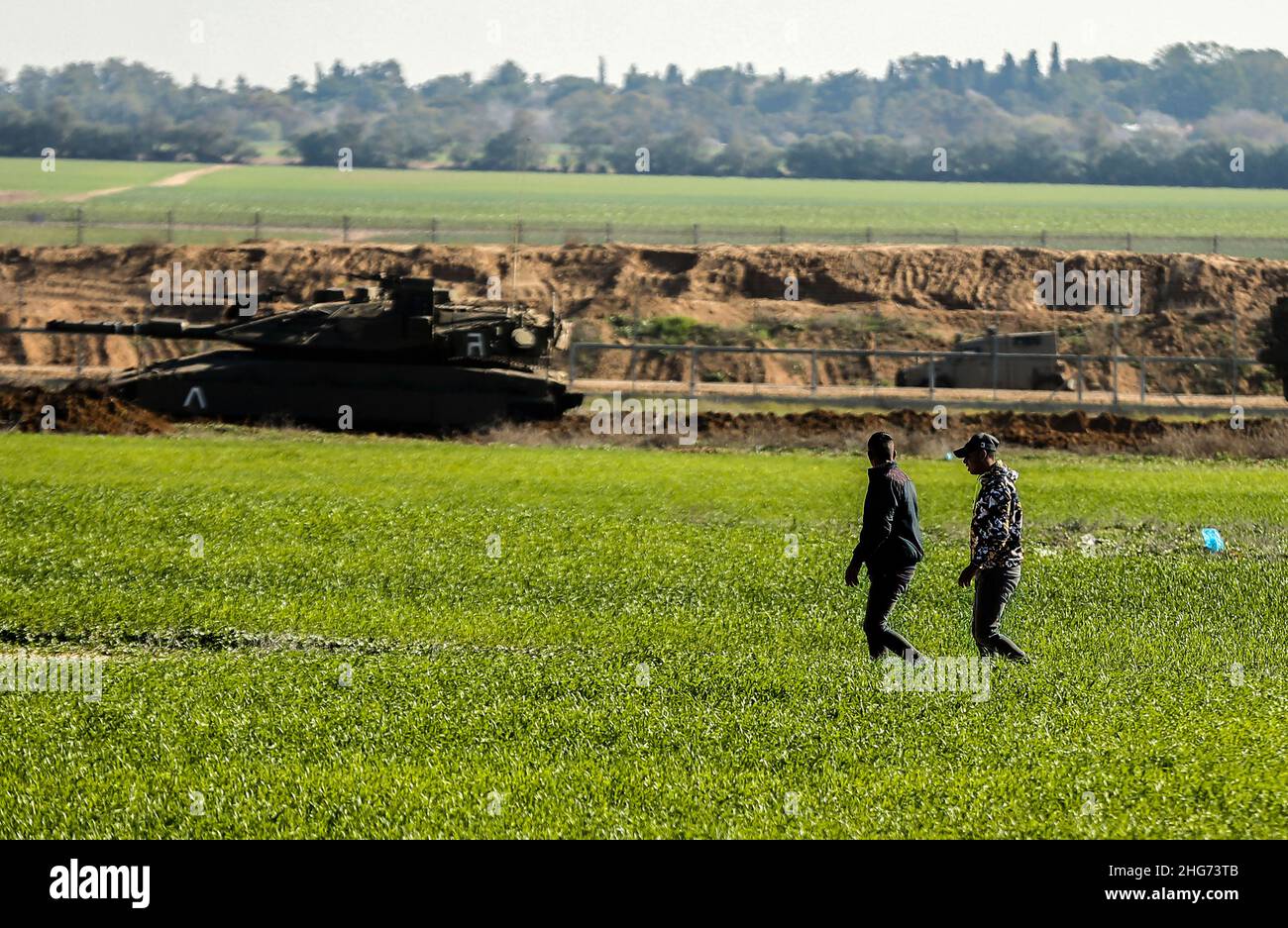 Gaza, Palestine. 18th Jan, 2022. Farmers work on a farm near the fence separating Gaza and Israel, while Israeli military vehicles bulldoze parts of Palestinian agricultural land in Khuza'a, east of Khan Yunis, in the southern Gaza Strip. Credit: SOPA Images Limited/Alamy Live News Stock Photo
