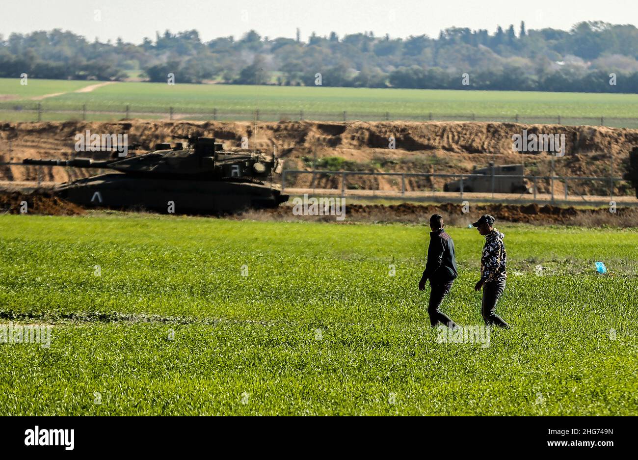 Gaza, Palestine. 18th Jan, 2022. Farmers work on a farm near the fence separating Gaza and Israel, while Israeli military vehicles bulldoze parts of Palestinian agricultural land in Khuza'a, east of Khan Yunis, in the southern Gaza Strip. (Photo by Yousef Masoud/SOPA Images/Sipa USA) Credit: Sipa USA/Alamy Live News Stock Photo