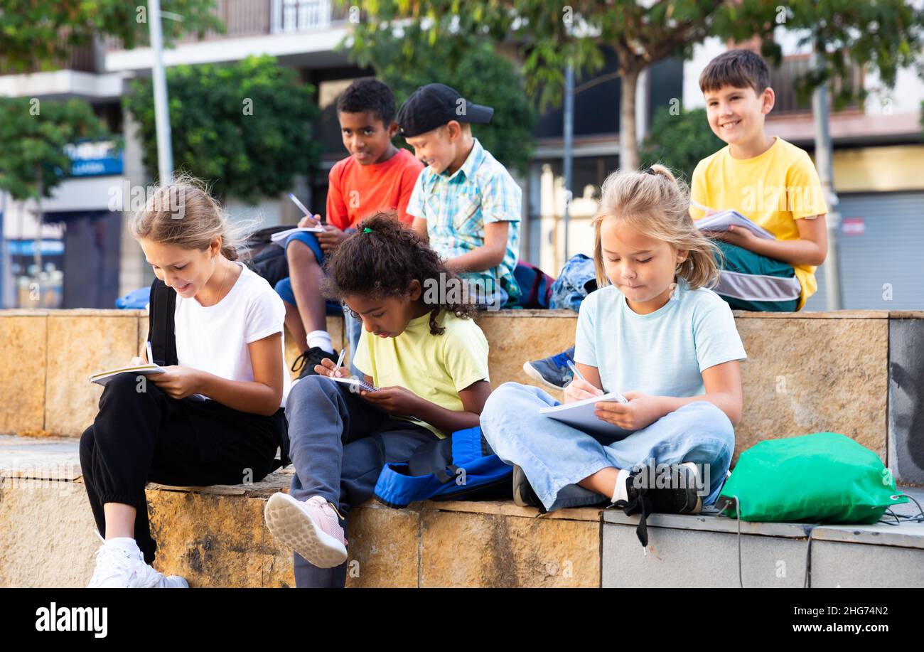Tweenagers studying outside school, writing in workbooks Stock Photo