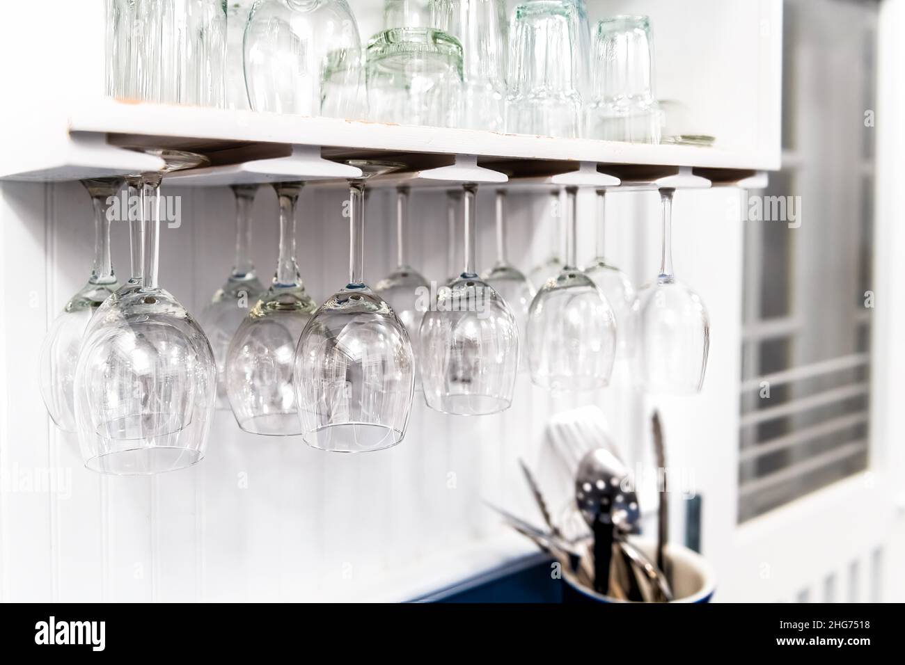 Closeup of modern kitchen interior design white shelf with upside down hanging empty wine glasses in room for storage of cups and nobody Stock Photo
