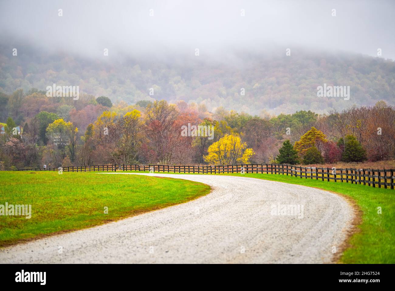 Farm curve dirt road picket fence in rural Virginia near Blue Ridge parkway mountains in autumn fall foliage season with idyllic landscape countryside Stock Photo
