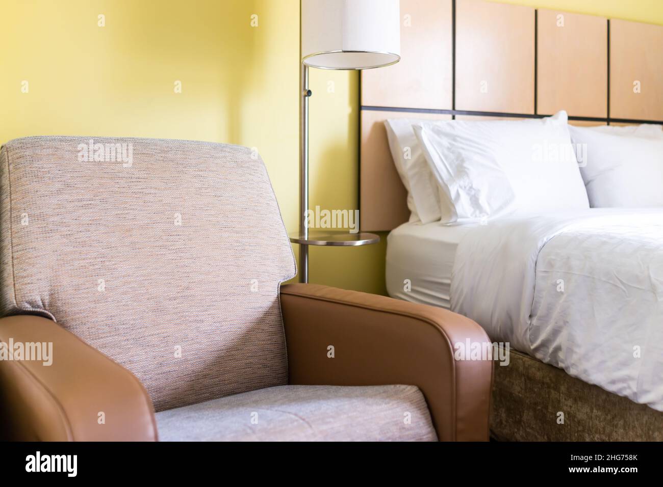 Bedroom room closeup of couch chair armseat with lamp white pillows sheets on mattress bed headboard in modern hotel motel room with nobody Stock Photo