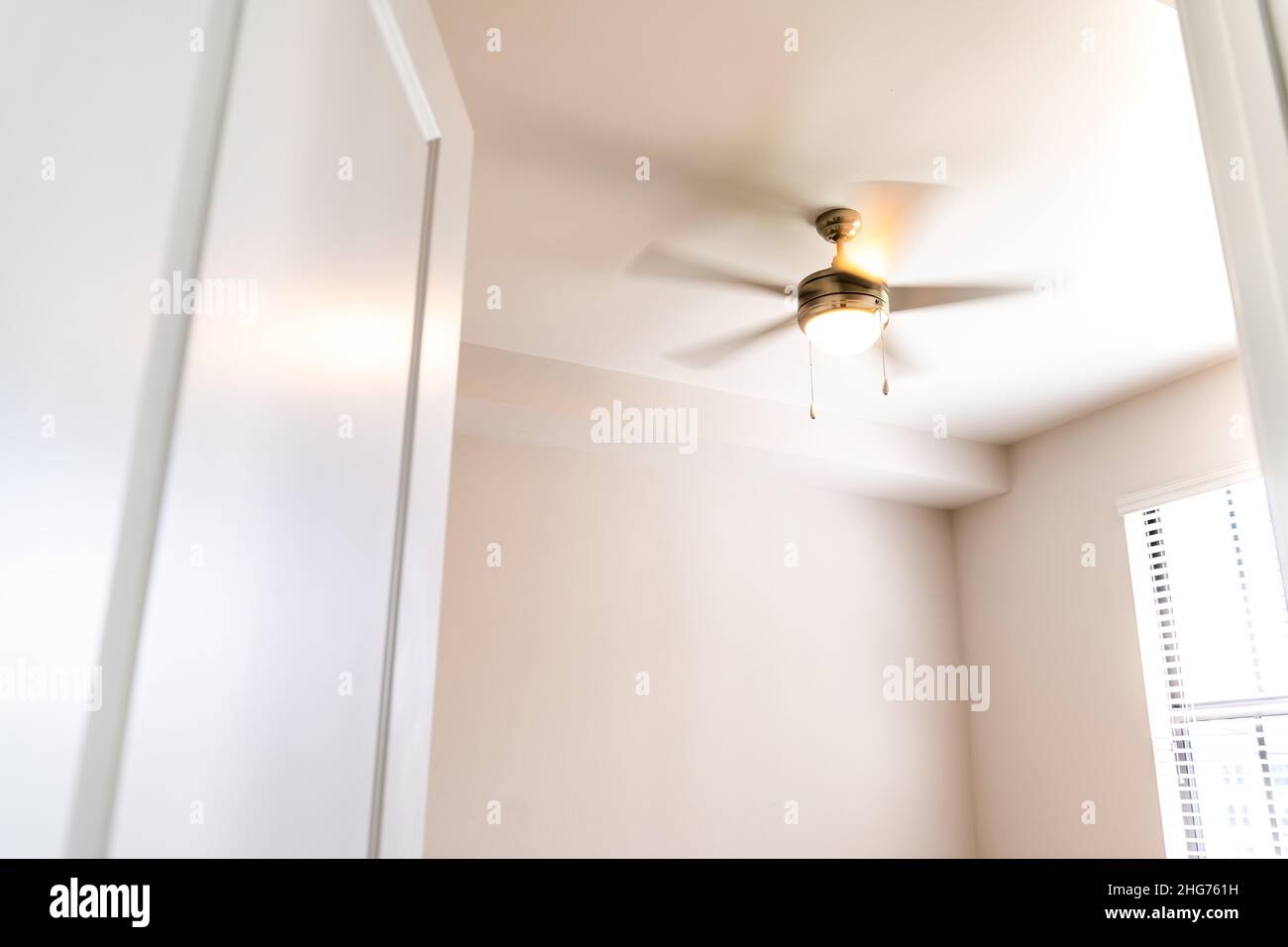 Empty bedroom room interior nobody looking up at lit illuminated yellow light spinning blurred motion ceiling fan open door window in new modern luxur Stock Photo