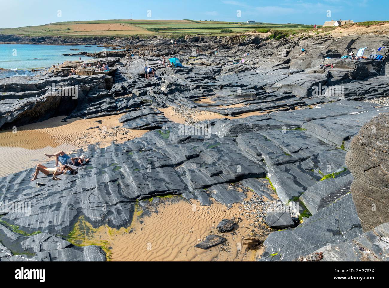 Trevose Head,Cornwall,England,United Kingdom-July 20 2021:Beachgoers and tourists sunbathe on ancient granite slate,at the beautiful beach cove, lappi Stock Photo
