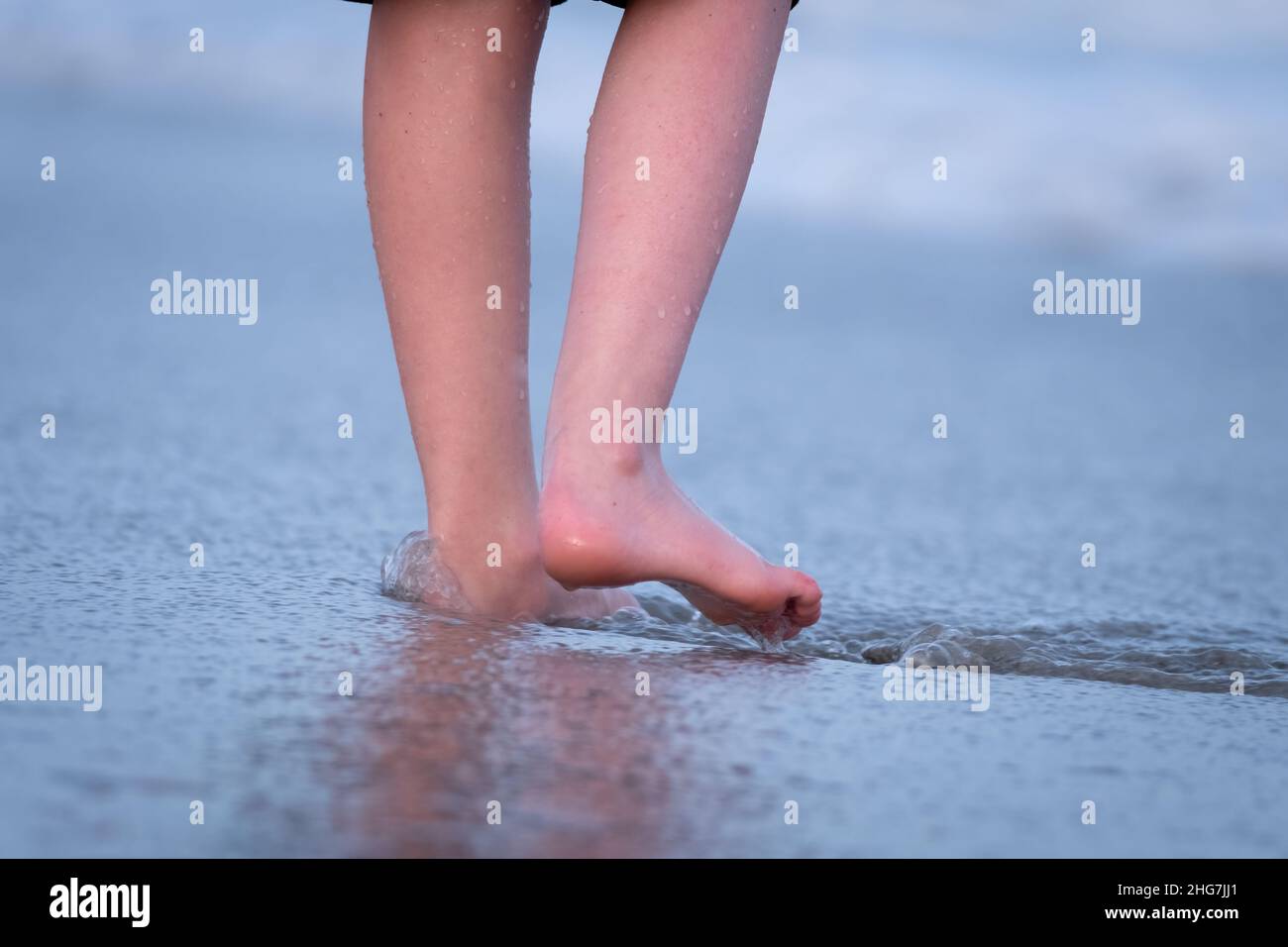 A child feels her feet sink in the sand as the water withdraws at the beach. Emerald Isle, NC. Stock Photo