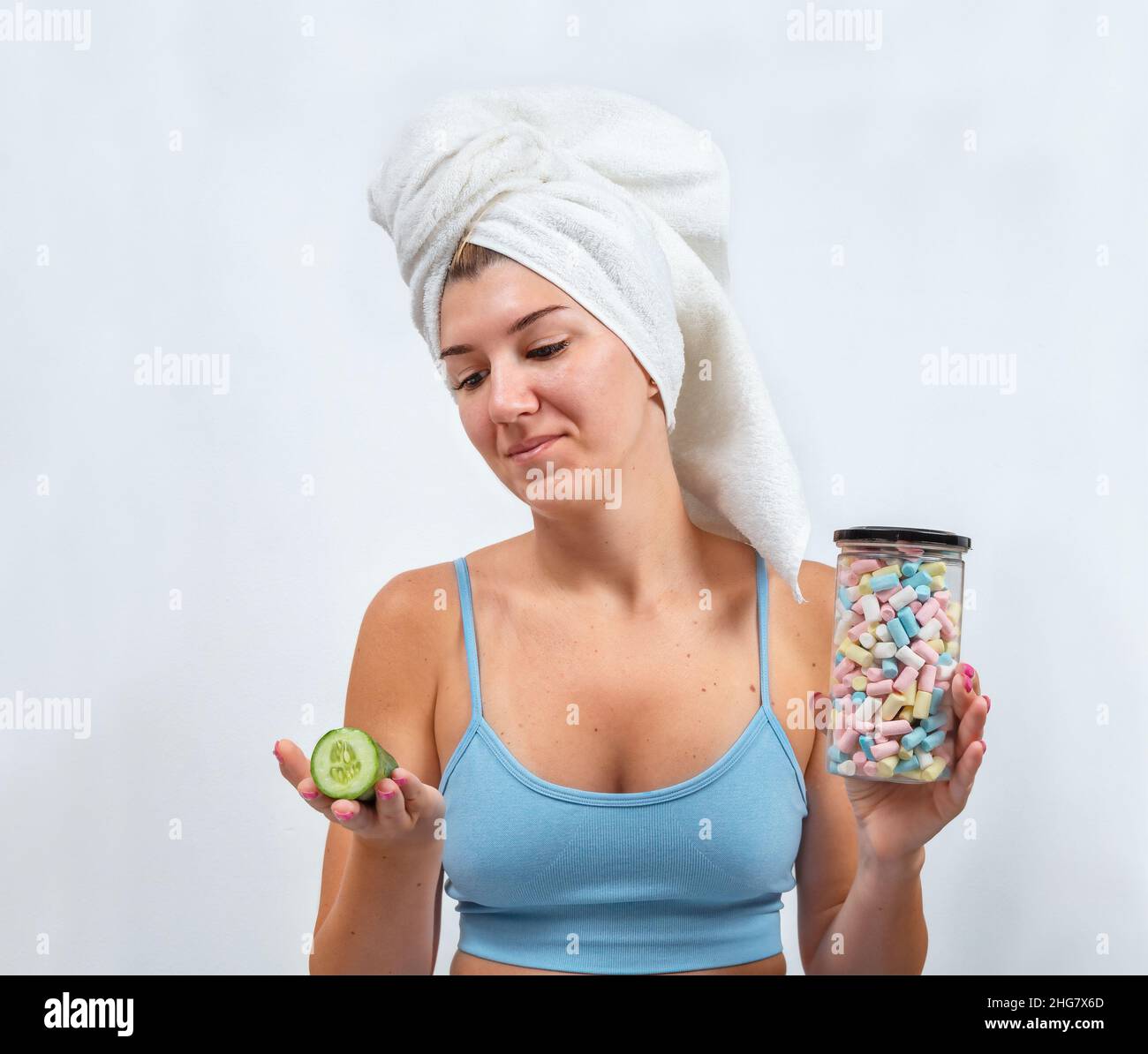 Young woman chooses between marshmallows and cucumber on gray background Stock Photo