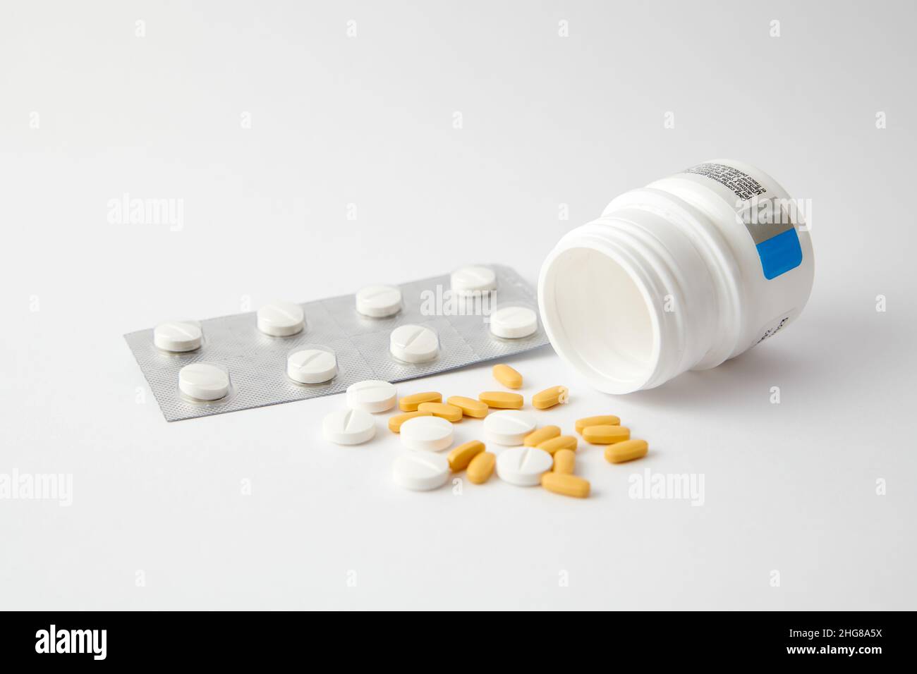 A closeup of white and yellow pills drop out of the pill bottle on the white surface Stock Photo