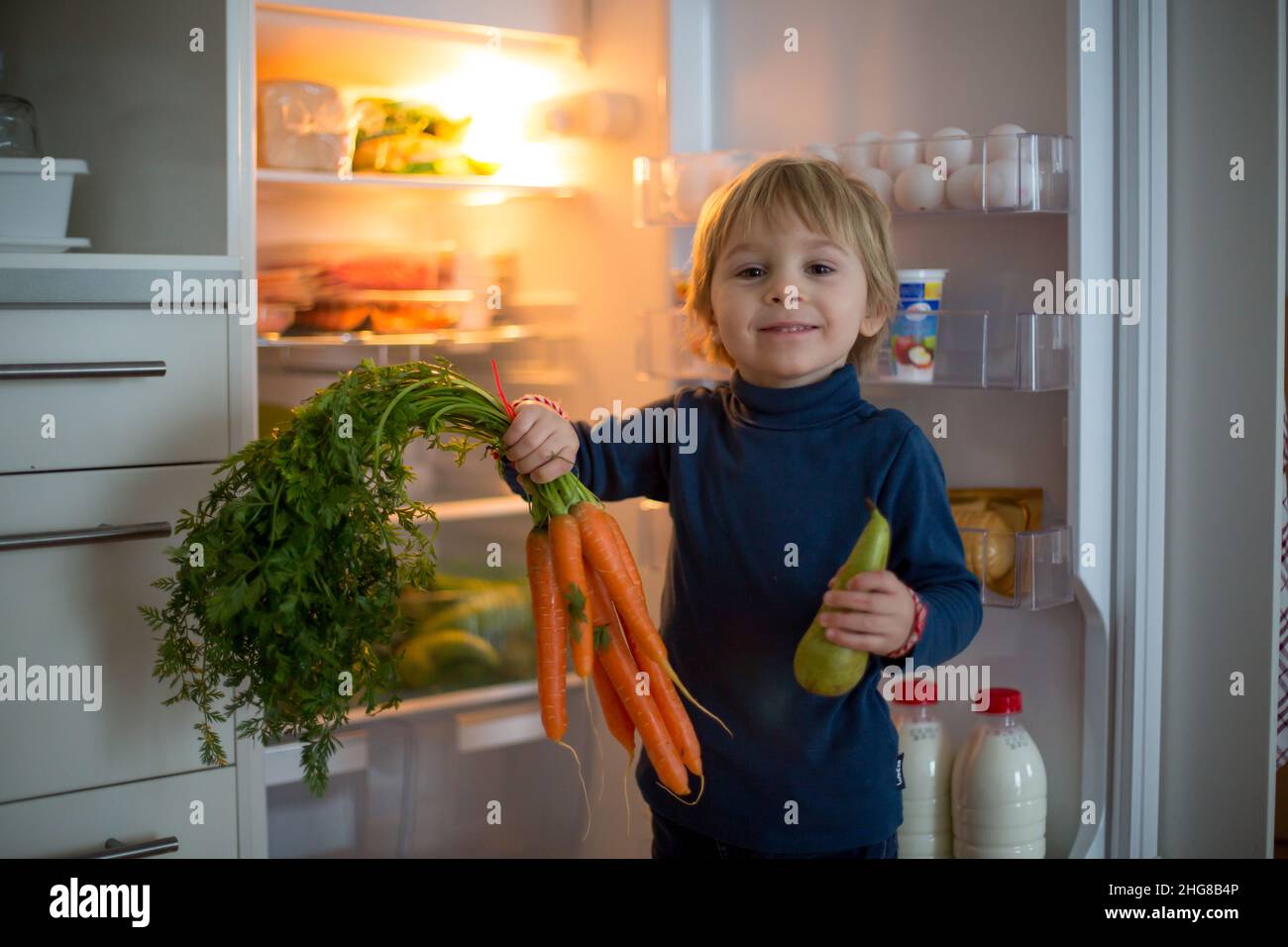 Cute toddler blond child, opening the fridge door and taking fruits and