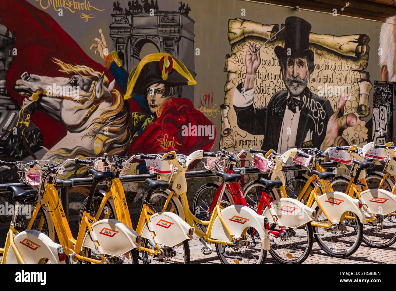 Rental bikes lined up in front of a wall of colorful imaginative graffiti with historical themes. Stock Photo