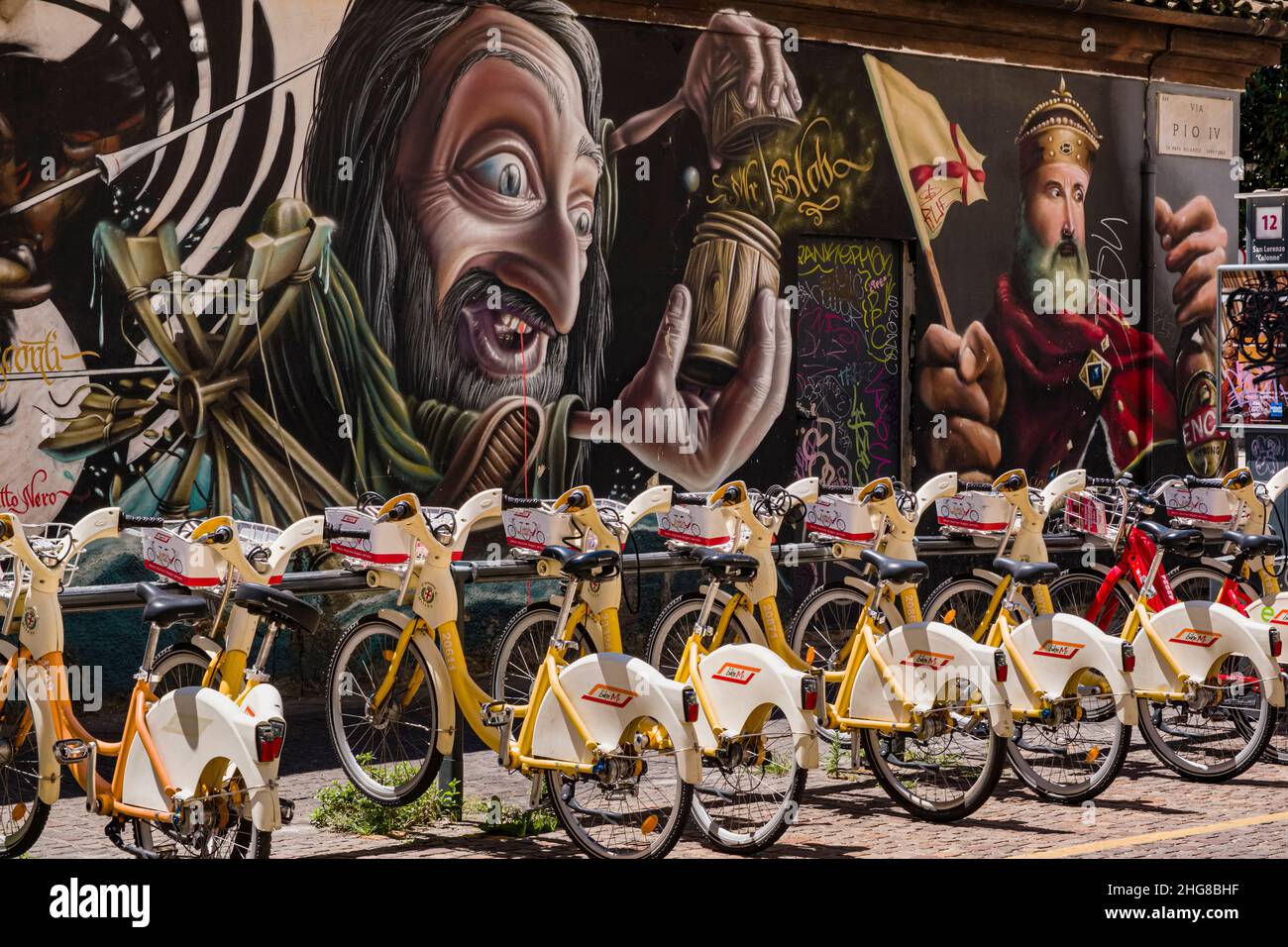 Rental bikes lined up in front of a wall of colorful imaginative graffiti with historical themes. Stock Photo