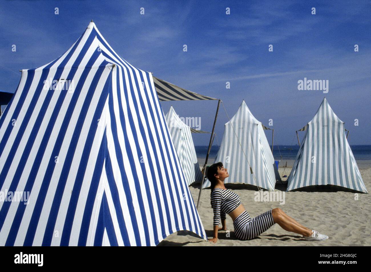 france Britany Dinard fashion shot young handsome woman sit on the beach in front tents graphic lines Stock Photo