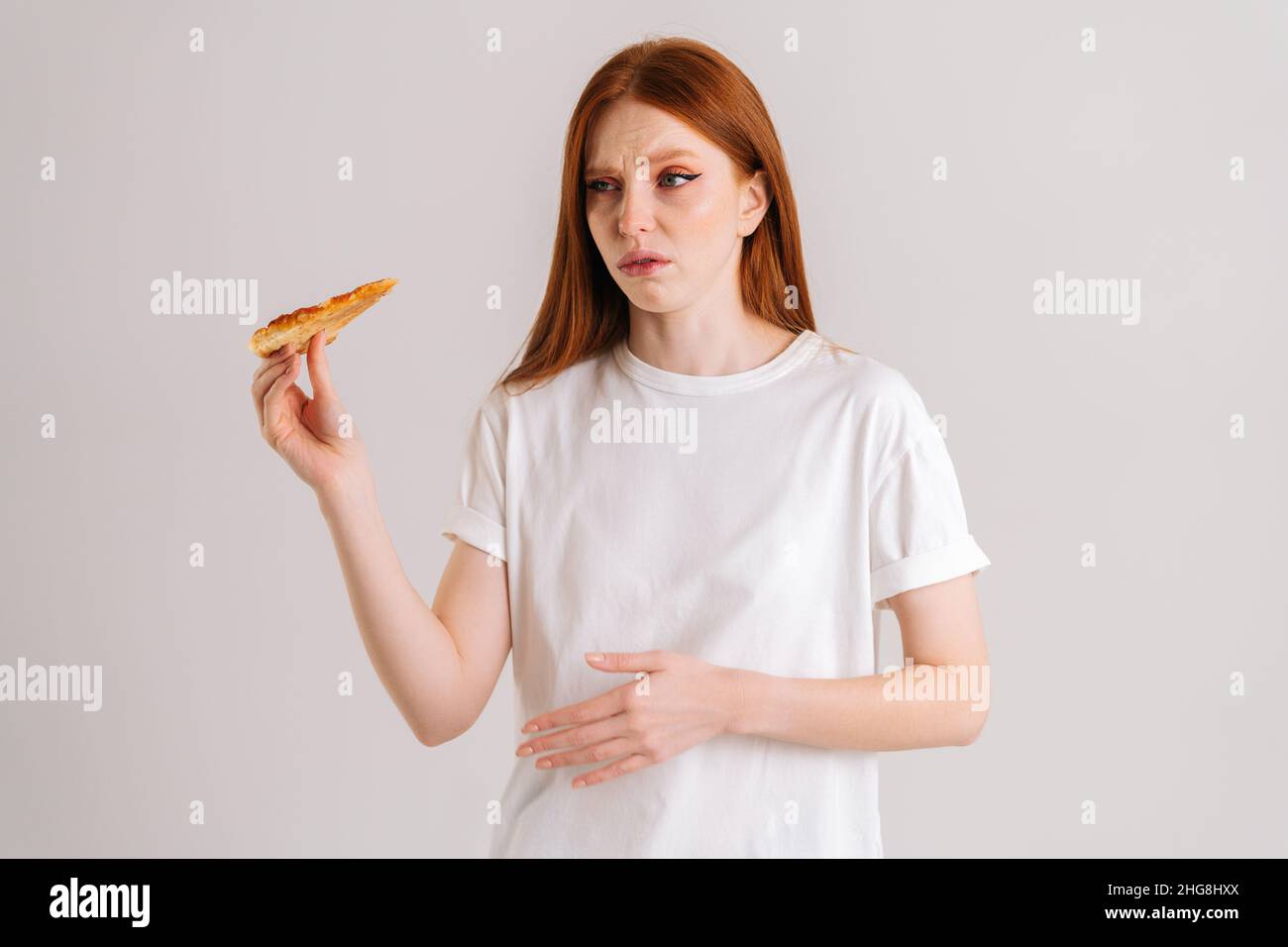 Studio portrait of sick crying young woman feeling pain in stomach after eating pizza, suffering