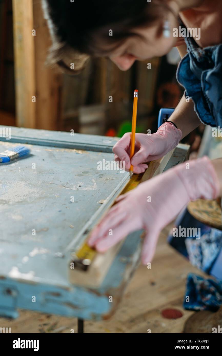 Close up view of hardworking professional carpenter woman hands working with ruler, making marks on wood. Reuse, reduce, recycle old things. Aware Stock Photo