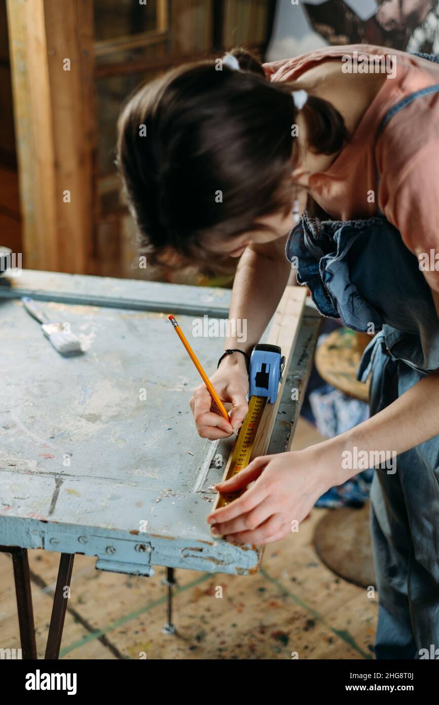 Close up view of hardworking professional carpenter woman hands working with ruler, making marks on wood. Reuse, reduce, recycle old things. Aware Stock Photo