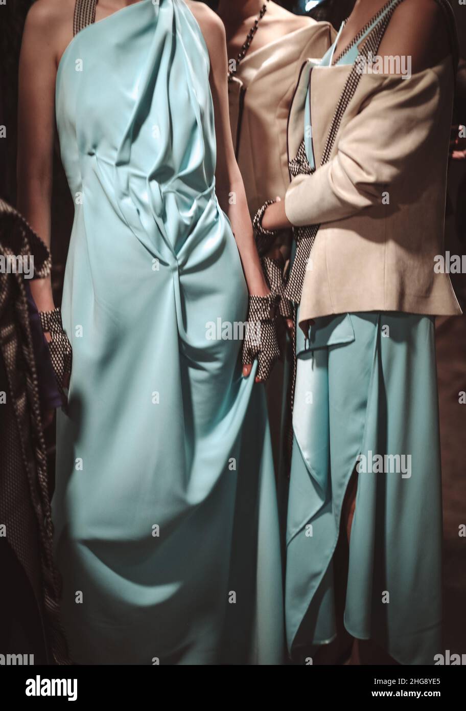 Two cropped female fashion figures in blue and beige stylish outfits, long dress and jacket on backstage Stock Photo