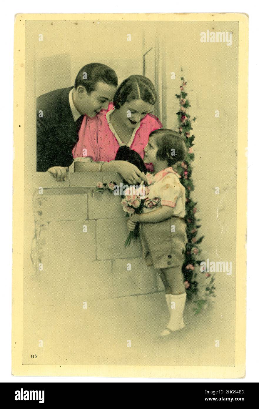 1920's French tinted greetings card photograph, kitsch, of child giving roses to mother and father, printed in France. Stock Photo