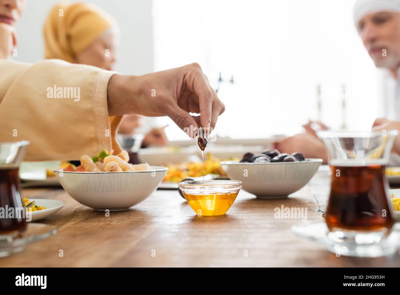 man dipping date into honey during dinner with multiethnic muslim