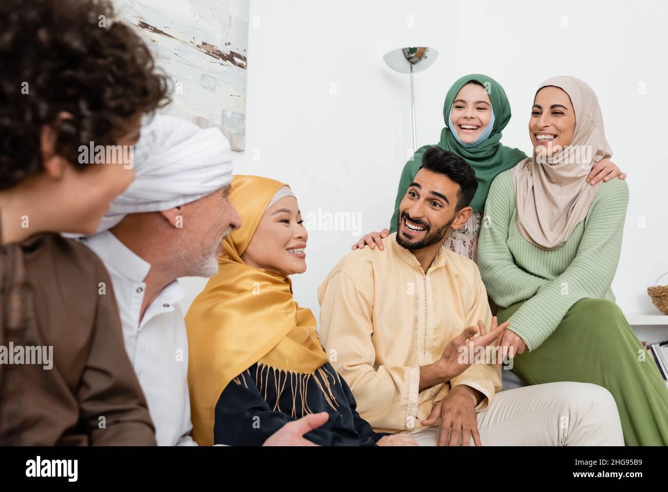 smiling arabian man pointing with hand while talking to cheerful multiethnic muslim family Stock Photo
