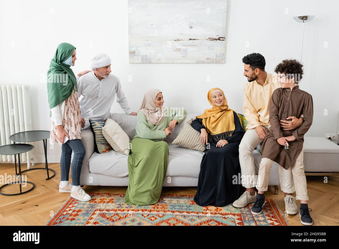 happy interracial women sitting on sofa near muslim family at home Stock Photo