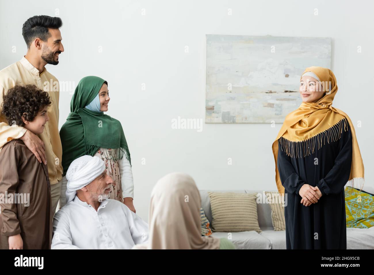 smiling asian woman in hijab looking at multiethnic muslim family at home Stock Photo