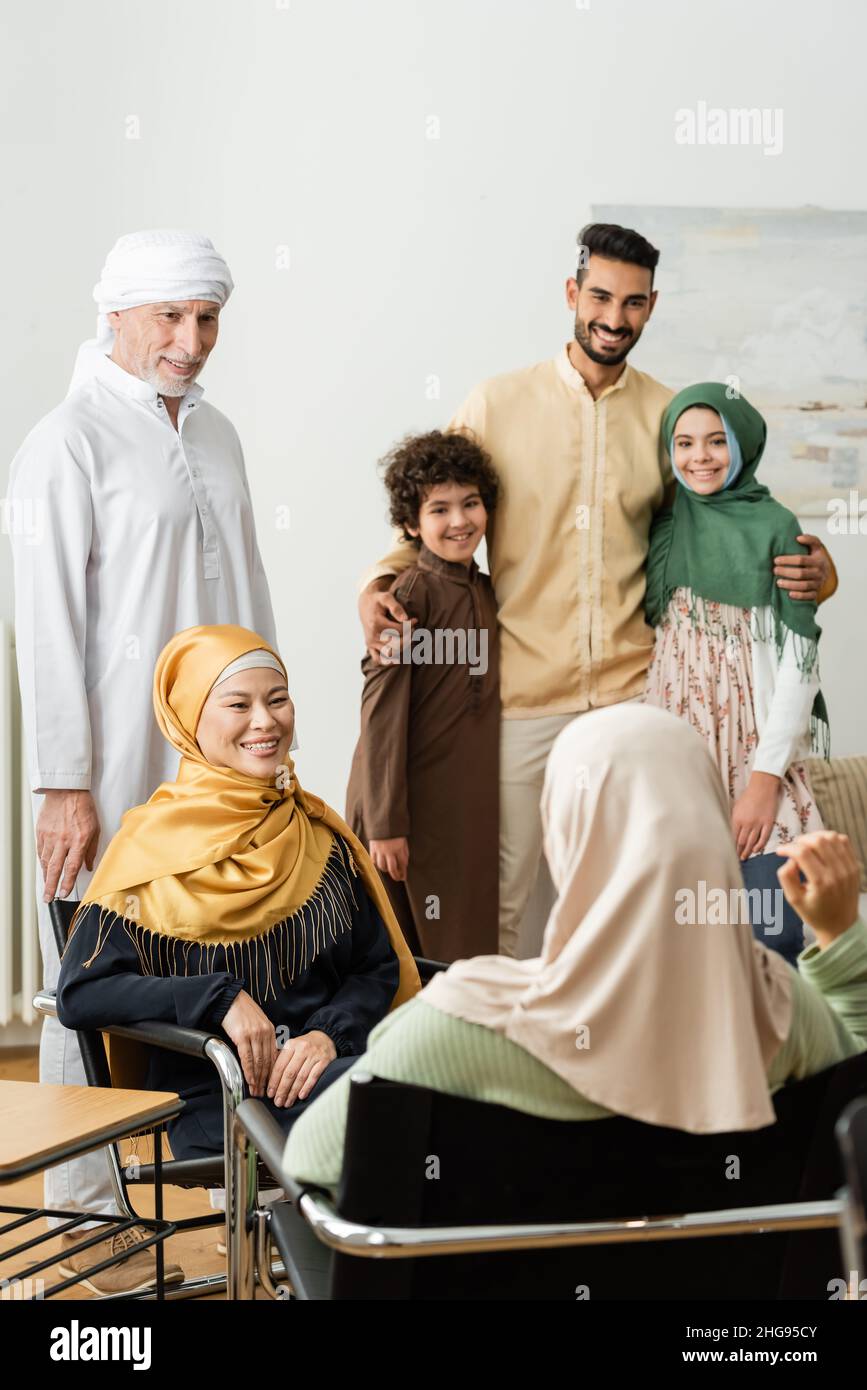 smiling arabian man embracing kids near multiethnic muslim family talking at home Stock Photo