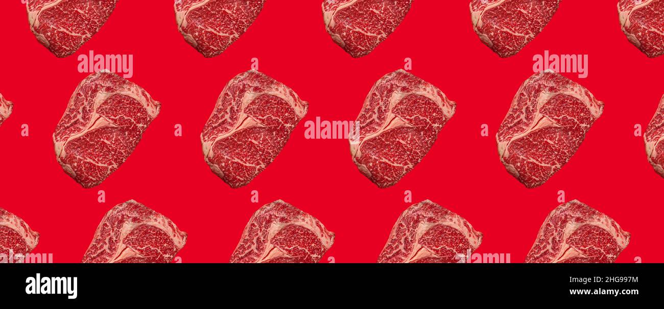 Pattern made of raw meat beef marbled prime cut steak Ribeye on red clean background Stock Photo