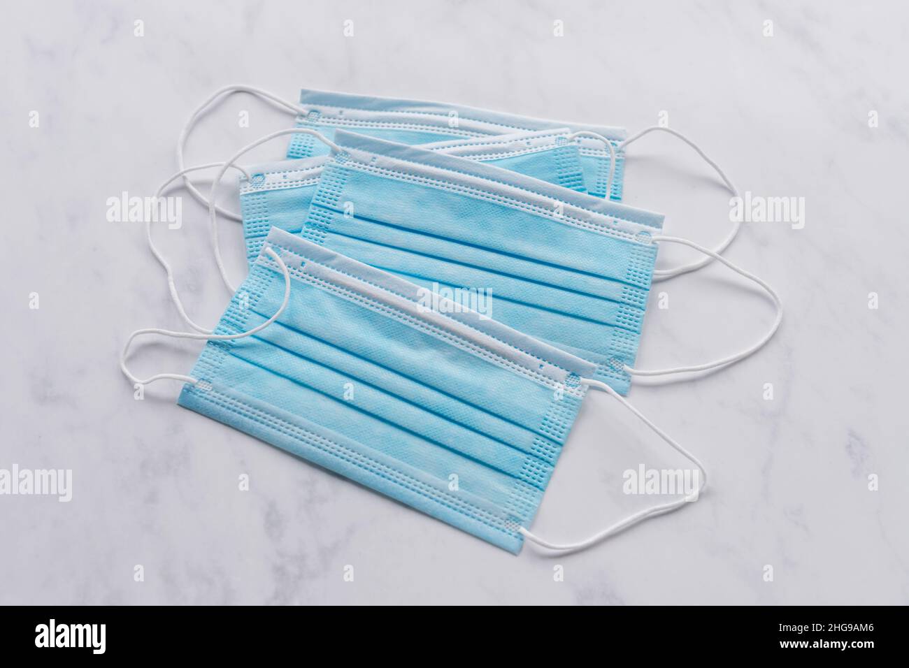 Four single use disposable blue face masks on white marble Stock Photo