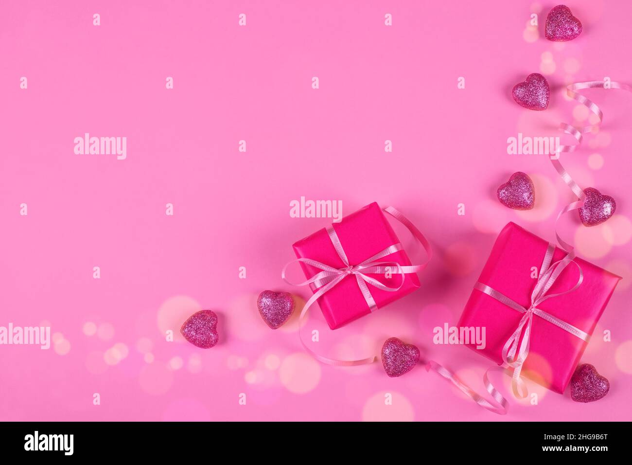 Overhead view of wrapped gift boxes with heart shaped ornaments on a pink background Stock Photo