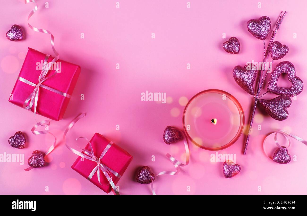 Overhead view of wrapped gift boxes with a candle and heart shaped ornaments on a pink background Stock Photo