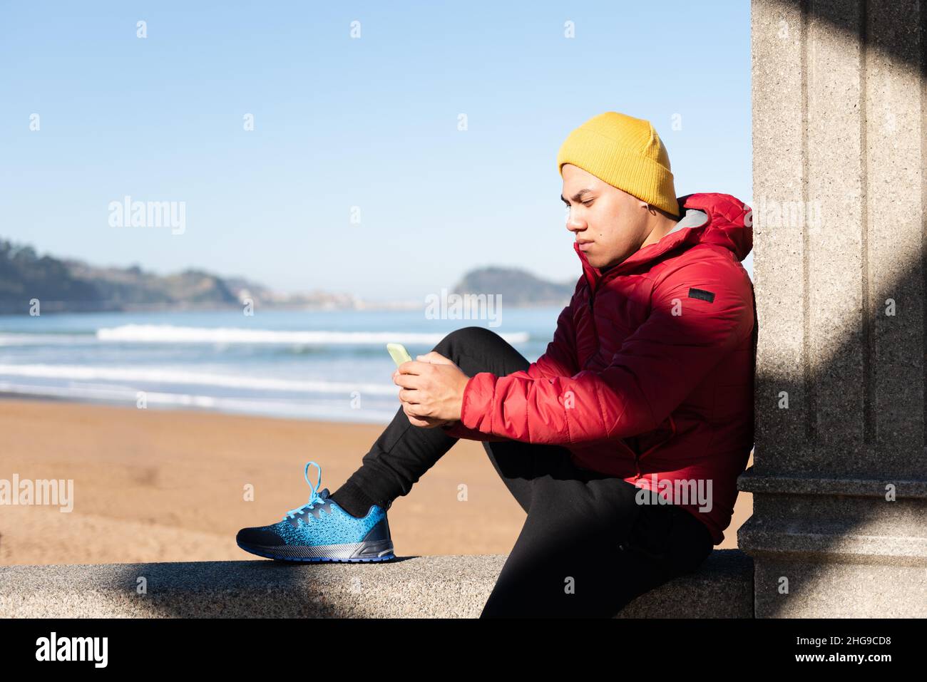 Latin man concentrated on his phone while sitting at seaside. Digital addiction concept. Stock Photo