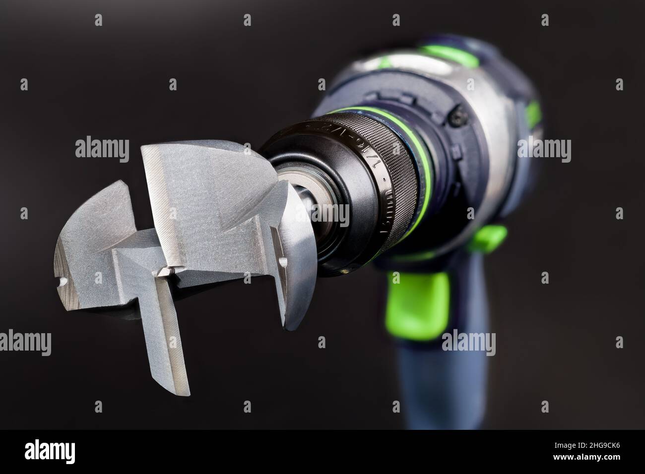 Steel Forstner bit in cordless drill on a black background. Metal professional cutting tool for boring flat bottomed holes in wood. Drilling  machine. Stock Photo
