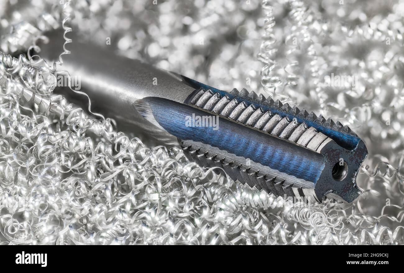 Spiral point straight fluted tap in a metal swarf heap. Beautiful steel tapping tool detail. Metric screw thread drill bit for creating threaded holes. Stock Photo