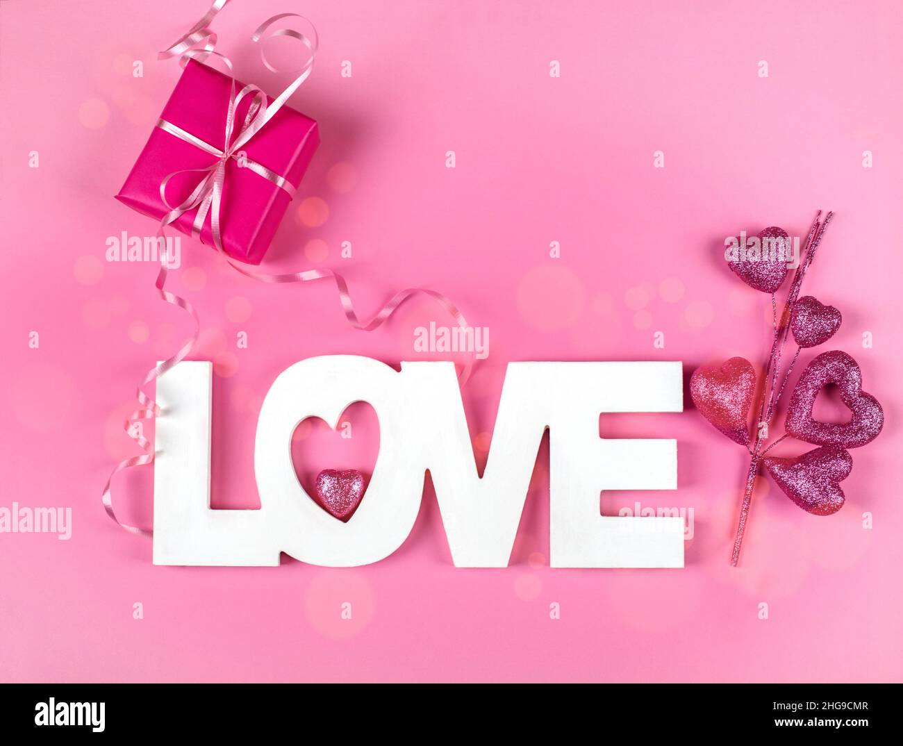 Wrapped gift box with the word Love and pink heart ornament on a pink background Stock Photo