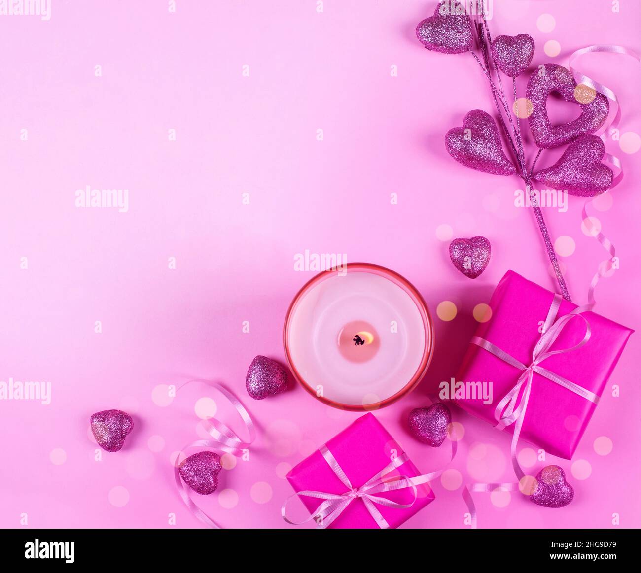 Overhead view of wrapped gift boxes with a candle and heart shaped ornaments on a pink background Stock Photo